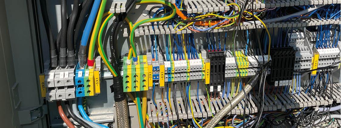 Close-up of terminal blocks, power cables, and densely wired electrical connections inside an industrial cabinet.